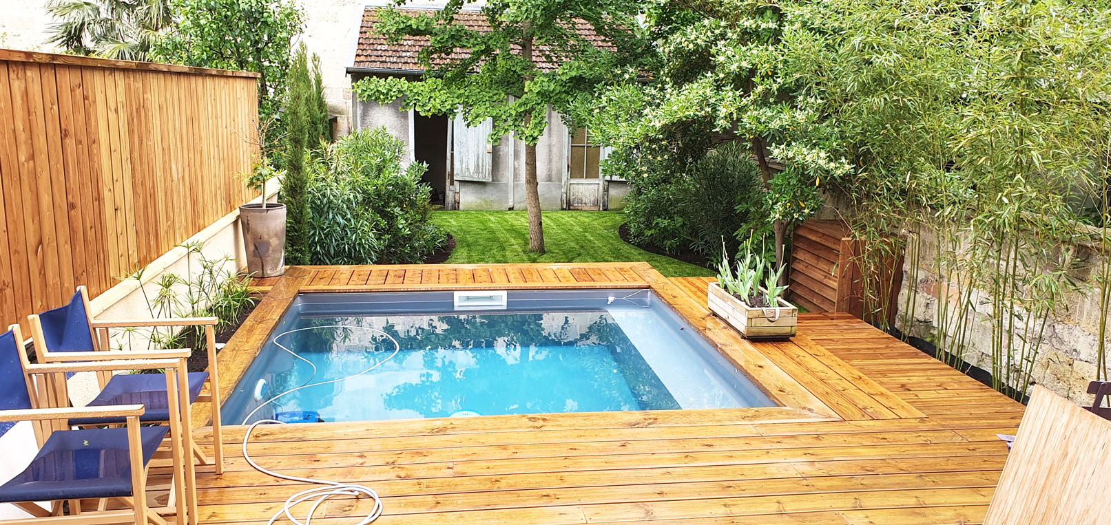 Photo d'un jardin d'échoppe réalisé à Bordeaux avec conception et aménagement. On peut y voir une piscine, avec une terrasse en bois, des jardinières intégrées et divers massifs
