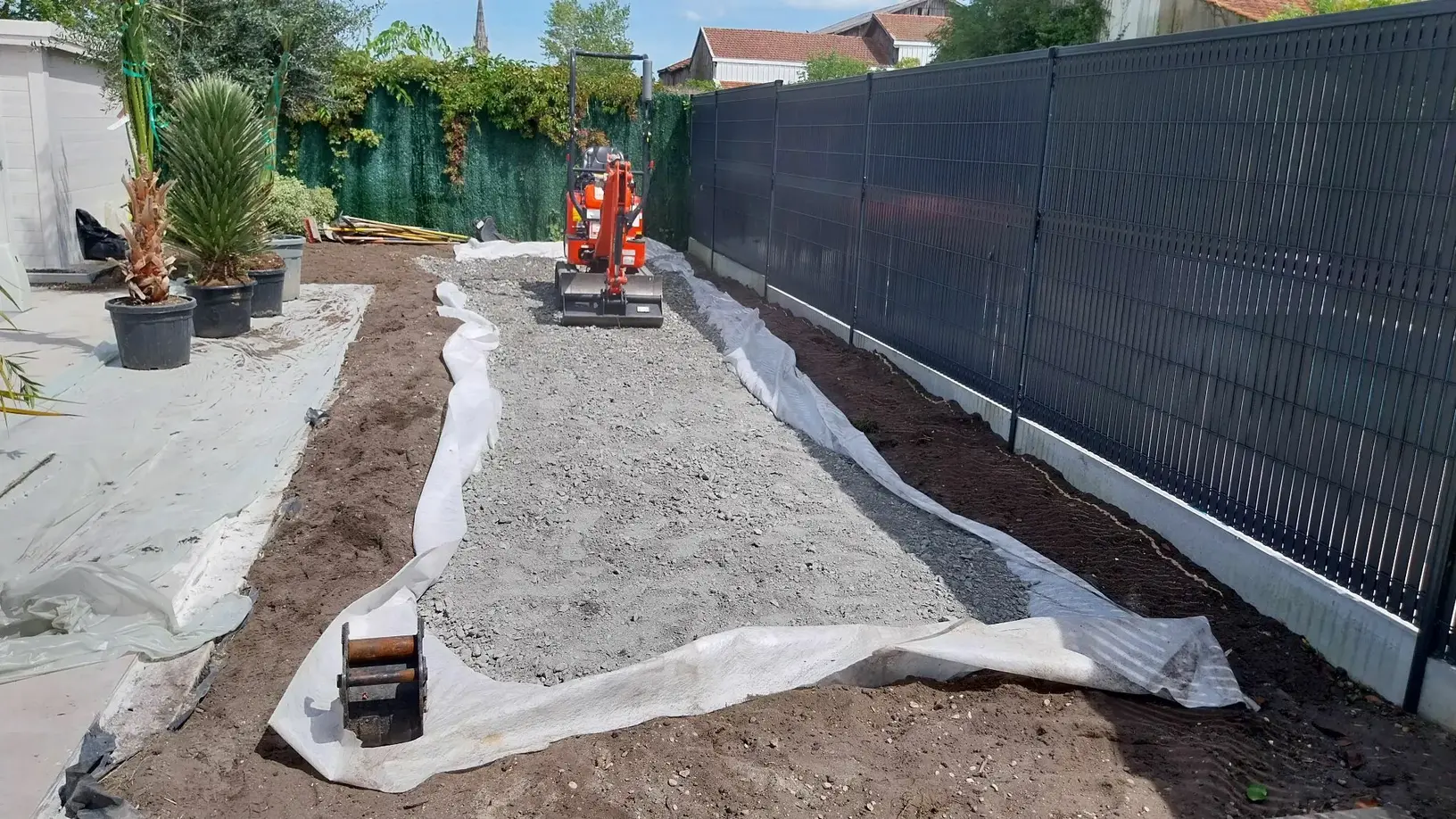 Petit jardin situé à l'arrière de la maison, où l'on voit une minipelle réaliser les travaux de terrassement pour la futur implantation du boulodrome