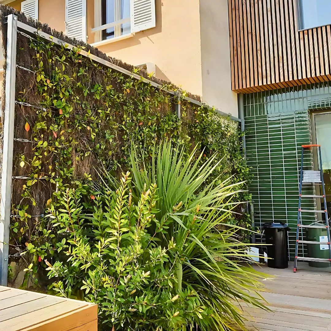 Photo d'une terrasse en bois avec un massif de plant exotique et l'aménagement d'une treille et la plantation de plantes grimpantes pour bloquer un vis-à-vis;