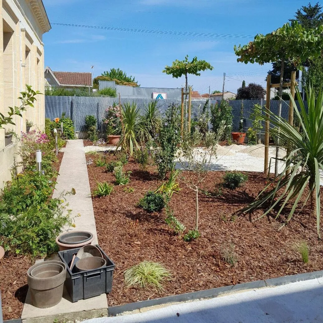 Photo du jardin prise depuis l'espace de stationnement. On voit les différents végétaux plantés et les espaces de circulation. 